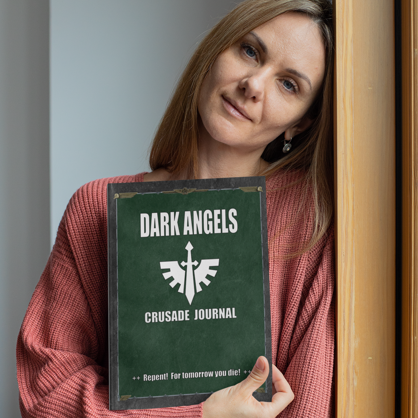 Woman holding a book titled 'Dark Angels Crusade Journal' with a green cover.